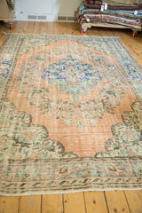 Distressed apricot orange Oushak rug corner with blue floral border and secured fringe.