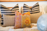 Antique Turkish rug fragment pillow features vibrant orange and red hand-knotted patterns.