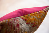 Pillow's raspberry red border joins textured hand-woven rug fragment with orange and red patterns.