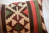 Geometric pattern of the Kilim pillow featuring beige, dark brown, coral, and olive green.