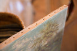 Antique painting canvas edge detail, showing securing tacks and soft green landscape tones.