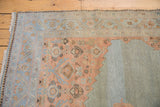 Distressed Malayer carpet corner showing pale terra cotta Herati motif and slate blue-grey border.