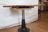 Reclaimed wooden tabletop edge, showing added supports and dark industrial metal base.