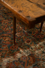 Detail of reclaimed wooden table's needle leg on a vibrant patterned rug.
