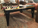 Side view of the black factory cart coffee table, showing wheel and rivet details.