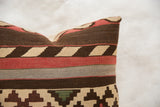 Hand-woven kilim pillow showing geometric patterns in earthy brown, brick red, and beige.