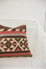 Geometric striped patterns in beige, brown, red, and green on an antique Kilim pillow corner.