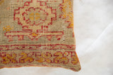 Textured edge of antique Turkish rug fragment pillow, showing geometric red and mustard pattern.