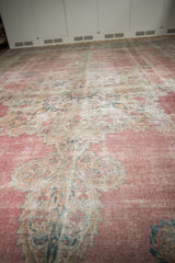 Angled view showcasing the worn texture and faded raspberry pink field of an antique Kermanshah rug.