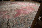 Angled view of Rococo outlines on the faded raspberry field of a distressed antique Kermanshah carpet.