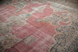 Intricate Rococo outlines in teal blue and ivory on the faded raspberry pink field of a distressed antique carpet.
