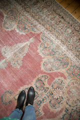 The ornate floral pattern and faded raspberry pile of a distressed antique Kermanshah carpet, shown for scale.