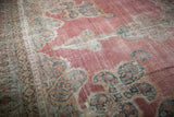 Angled perspective on the distressed Rococo outlines and faded raspberry pink field of an antique rug.