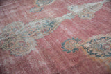 Low pile texture of a distressed Persian rug showing faded raspberry, ivory, and sky blue floral details.
