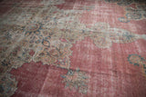Angled view across the distressed low pile of an antique Kermanshah rug's ornate medallion.