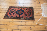 Vintage Lilihan rug's primitive navy blue medallion on dark blush field with scrolling leaves.