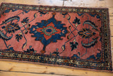 Corner of vintage Lilihan rug: dark blush field, scrolling leaves, navy border, tattered fringe.