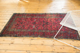Corner of a vintage Lilihan rug showing vivid floral vinery and wear on the fringed edge.
