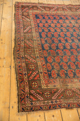 Antique Kurdish rug corner showing chocolate bronze border, red paisley motifs, and tattered edge.