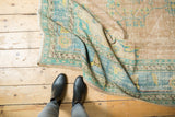 Distressed vintage Oushak carpet with worn texture, pale aqua and beige border, and scrolling tendrils.