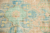 Distressed Oushak rug's faded aqua, peach floral patterns, worn pile, and visible foundation.
