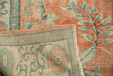 Distressed Oushak carpet pile texture, faded tangerine orange and mint green, revealing the rug's back.