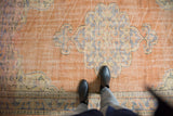 Distressed vintage Oushak rug with scalloped medallion, trefoil motifs, and warm orange field.