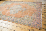 Distressed Oushak rug corner showing dusty peach field, meandering vine and pearl motif borders.