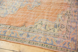 Oushak rug's muted peach and pale blue meandering vine and pearl borders.
