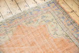 Distressed vintage Oushak rug corner showing dusty orange peach field, ivory spandrel, blue border.