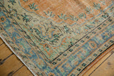 Distressed Oushak rug corner with worn orange field, ivory, and blue geometric borders.