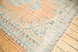 Distressed Oushak rug corner, showcasing worn texture and peach, mint curvilinear motifs.