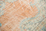 Distressed Oushak texture, showing worn dusty apricot pile, visible foundation, and faded blue Rococo details.