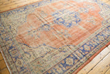 Distressed Oushak carpet featuring worn pale red pile, foundation showing through, blue floral motifs.