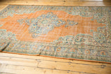 Distressed vintage Oushak rug showing low shorn pile, tangerine field, and European-style vinery.