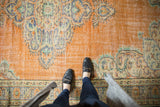 Distressed tangerine field and Rococo vinery texture of the vintage Oushak rug.