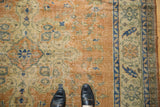 Distressed Oushak carpet field, apricot, ivory, navy floral texture, with black shoes.