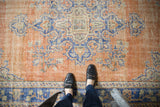 Vintage distressed Oushak rug with low shorn pile, terracotta, and blue medallion elements.