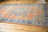 Vintage distressed Oushak rug with low shorn apricot terracotta pile and blue border.