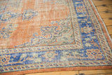Distressed Oushak rug corner showing low shorn apricot terracotta pile and blue border.