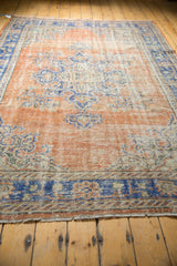Fringed bottom edge of distressed Oushak rug, showing apricot field and blue border.