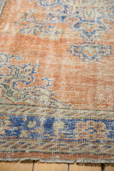 Close-up of vintage distressed Oushak rug with low pile, apricot terracotta, blue, and ivory patterns.