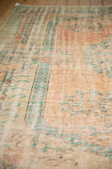 Distressed vintage Oushak rug texture showing low pile, pale blush, and aqua green tones.