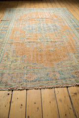 Distressed Oushak rug end featuring low pile, short fringe, soft apricot, blue tones.