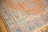Distressed vintage Oushak rug with low shorn pile, apricot field, and geometric blue border.