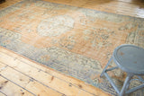 Vintage distressed Oushak carpet corner with faded apricot field, geometric blue border.