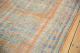 Distressed pile of vintage Oushak rug runner featuring terracotta, blue, and mint gul motifs.