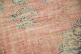 Distressed blush rose Oushak rug showing faded floral details and visible foundation.
