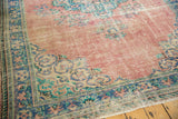 Corner of Oushak rug, showing blush rose field, worn texture, and fringe.