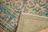 Distressed Oushak rug corner revealing worn blush rose pile and hand-knotted foundation.